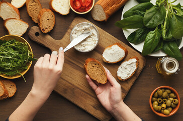Preparing healthy vegetarian bruschettas on dark rustic wooden table. Top view on female hands...