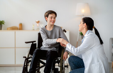 Disabled people healthcare support concept. Doctor holding hands of handicapped teen boy in...