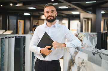 Portrait of a ceramic tile seller. The seller stands against the background of a large assortment...