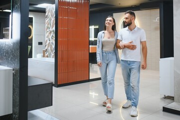 Young couple choosing new bathroom furniture at the plumbing shop with lots of sanitary goods