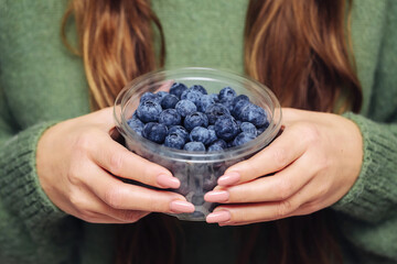 Girl holding a bowl of blueberries. Plastic food container. Healthy eating with berries rich in...