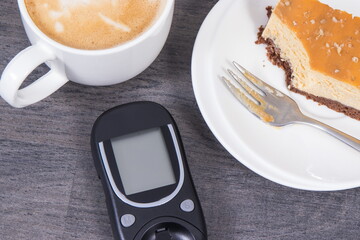 Glucometer using for sugar level control, portion of sweet cheesecake and cup of coffee with milk....