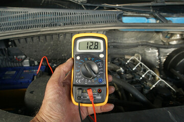 Checking the voltage of the battery installed in the car. The master electrician checks the voltage...