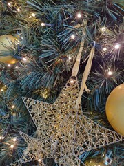 Detail of Christmas tree decoration with golden color scheme. Ball ornaments and star at green fir tree. Magic background of christmas decoration in sparkling holiday lights. Vertical image