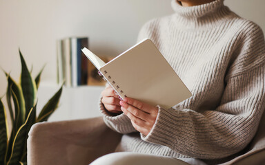 Cozy indoor reading session with a woman in a knit sweater holding an open notebook