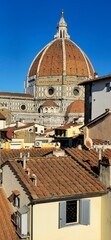 Fototapeta premium Florence, Italy - November 24, 2024: The iconic dome of Florence Cathedral, designed by Brunelleschi, rises above the historic terracotta rooftops under a vibrant blue sk
