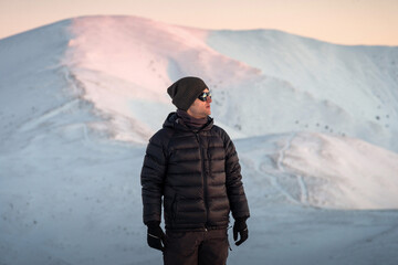 Young hiker man in outdoor gear enjoying sunset view in snowy mountains.