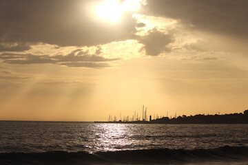 The silhouette of a city by the sea with an evening sky and the sun shining
