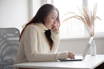 Woman focused on work at a desk with laptop in a bright and airy room surrounded by plants