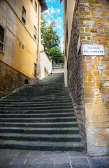 Nestled in the Florence Historic Center district, Florence, Italy, and near the Arno River, the Pitti Palace and the Ponte Vecchio, a romantic staircase descends to an Italian street on a summer day.