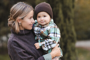 Smiling mother holding baby girl 2-3 year old wearing knitted hat and sweaters outdoor. Motherhood.