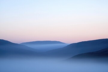 Fototapeta premium A scenic view of a foggy mountain range at sunset, suitable for travel or nature-themed projects