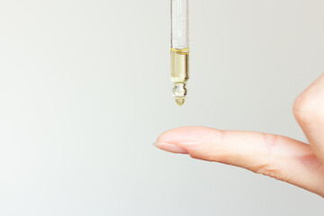 A woman applying a moisturizing serum from a pipette to her index finger for application to the...