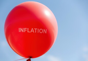 Red balloon with inflation lettering floating against blue sky representing economic crisis