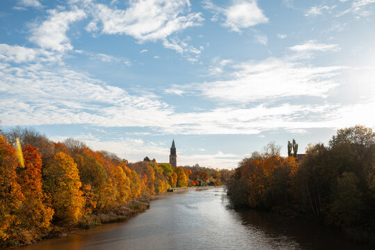 Autumn river landscape with church tower and colorful trees
