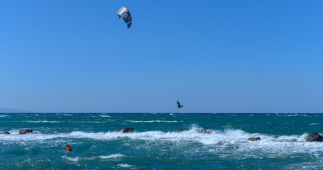 Sun-kissed kitesurfers ride the waves on a vibrant blue ocean during a windy afternoon by the shore