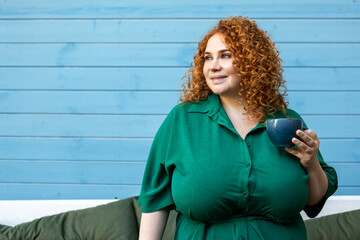 Beautiful Plus Size Woman with Red Hair Drinking Coffee or Tea. Curvy Female Model in Green Dress...