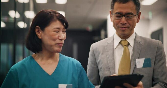 Nurse, doctor and walking with tablet in hospital for health management and staff service delivery. Medical administration, japanese people and digital policy for quality assurance or clinic schedule