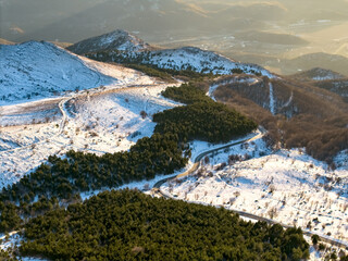 Aerial view of winter landscape with mountain road. Mountain hills covered with dense forest and...