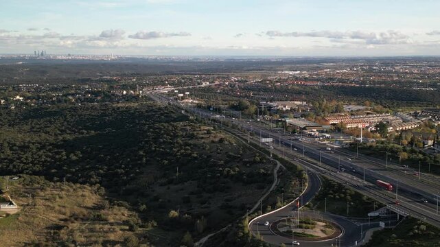 Aerial drone view of Torrelodones, a municipality in the northwest of the Autonomous Community of Madrid, Spain with cars on the A6 highway with Madrid in the background