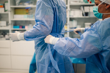 Medical professional ties surgeon's gown for surgery in sterile room.