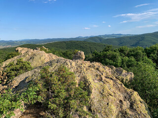A rocky outcrop, adorned with vibrant green moss, overlooks a breathtaking panorama of rolling hills and distant mountains. 
