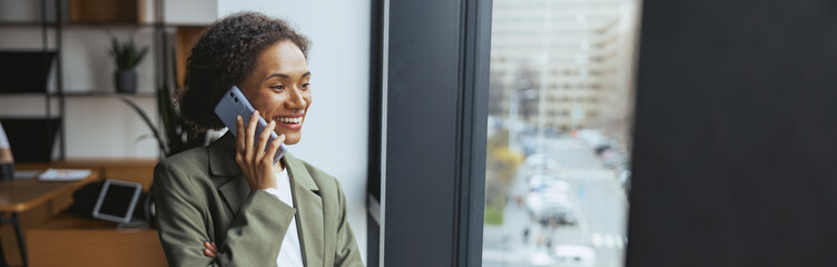 Whitecollar worker chatting on cell phone by window in office building