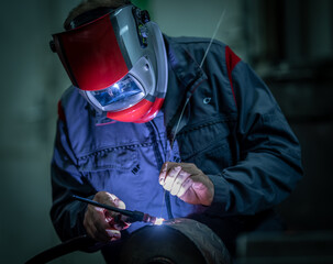 A worker manually welds steel and stainless steel components using TIG technology, detail of an electric arc.