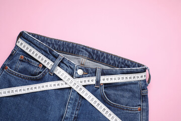 Jeans and measuring tape on pink background, top view. Space for text