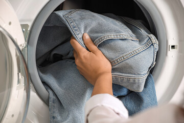 Woman putting dirty jeans and other denim clothes into washing machine, closeup