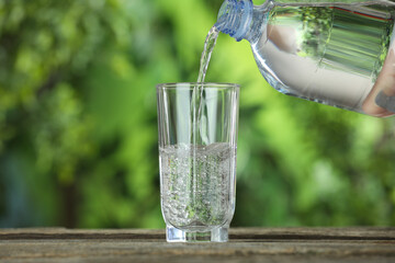 Pouring soda water in glass at wooden table outdoors