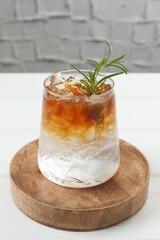 Refreshing espresso tonic drink with rosemary on white table, closeup
