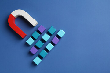 Magnet attracting colorful cubes on blue background, flat lay. Space for text