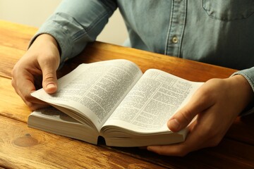 Naklejka premium Man reading Holy Bible in English language at wooden table, closeup