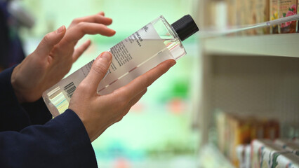 Close-up hands hold transparent bottle of body wash or shampoo. Customer reading label with...