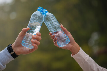 Close up cropped of woman and man two hands horizontal holding water bottles and clinking