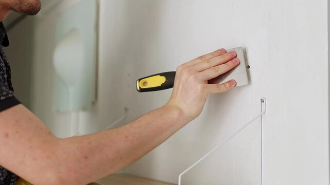 A young man covers a hole in the wall with putty with a spatula.