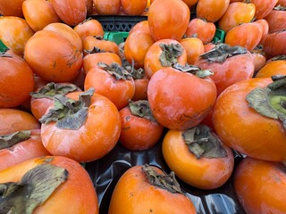 Persimmon fruit sales aisle at the greengrocer counter. A view of a pile of giant fuyu persimmons,...