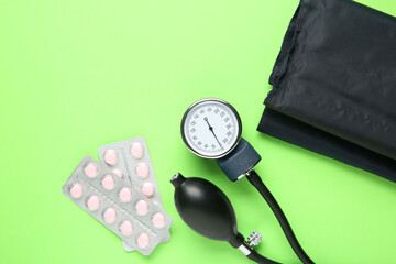Blood pressure measuring device and pills on green background, top view. Space for text