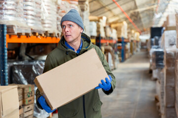 Fototapeta premium Warehouse worker carrying large box of goods in a warehouse