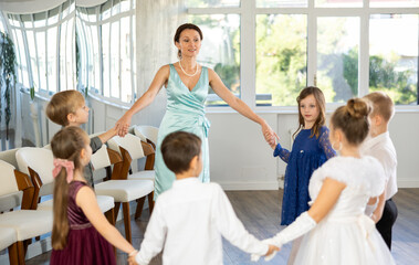 Group of happy preteen kids in festive clothes playing round dance in classroom