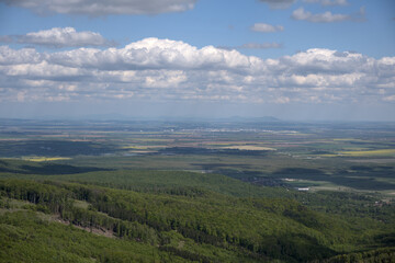 Obraz premium A close-up view of lush green hills meeting a flat countryside, with soft sunlight and a backdrop of fluffy clouds.