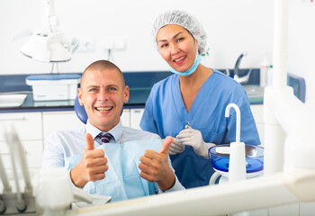 Portrait of a smiling asian woman dentist with a satisfied young man patient sitting in a dental chair in the clinic office