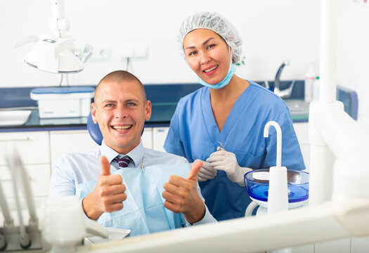 Portrait of a smiling asian woman dentist with a satisfied young man patient sitting in a dental chair in the clinic office