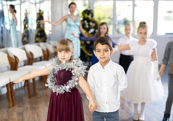 Pleased schoolboys and schoolgirls of primary classes standing in row performing dance position in...
