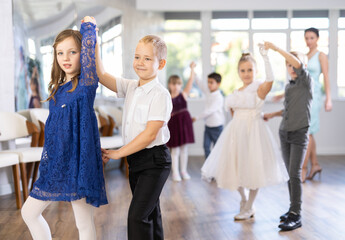 Joyful schoolboys and schoolgirls of primary classes training valse dance in events salon
