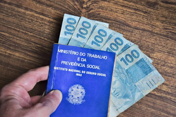 Brazilian work card on brazil money banknotes. Man's hand holding work card and 100 reais notes