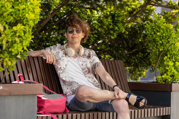 Happy Caucasian man tourist with backpack sitting on bench on urban city street relaxing, taking a...