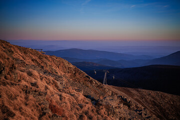 Rocky mountaintop slope with lift at sunset.