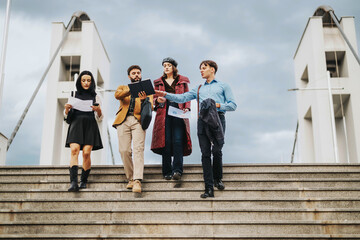 A group of young business people walking down city steps, engrossed in conversation and reviewing...